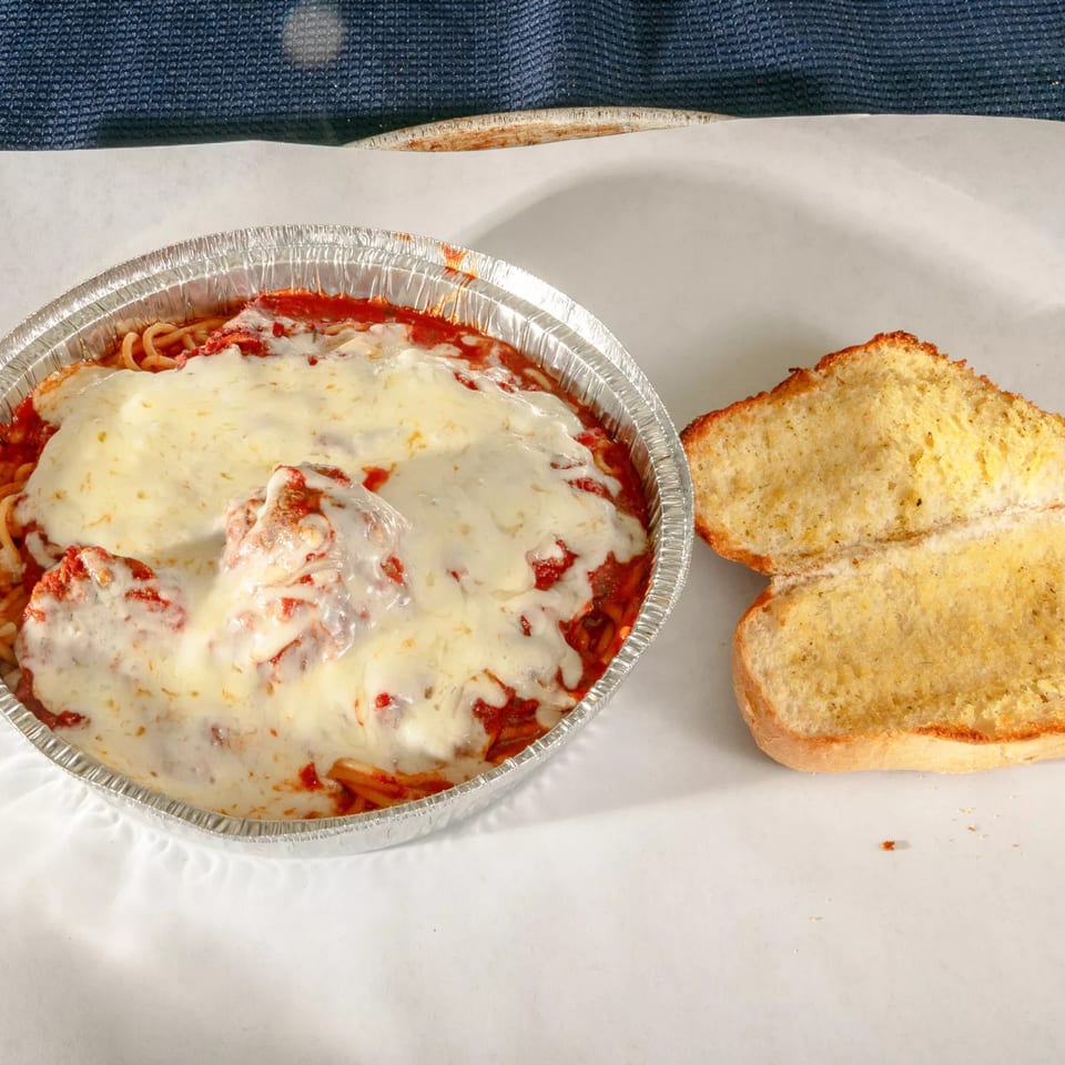Zeda's Pizza baked spaghetti with meatballs and melted cheese in a foil pan, with garlic bread.