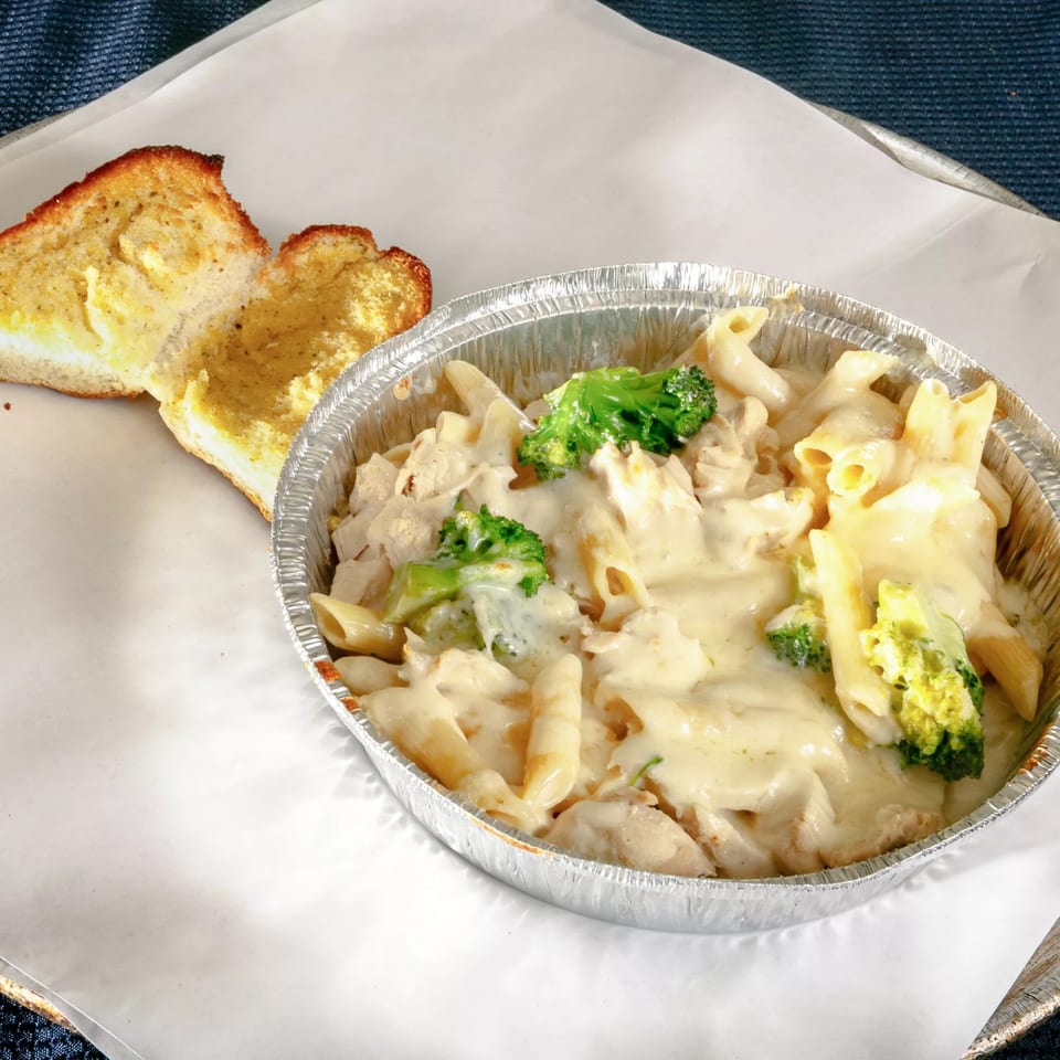 Creamy pasta with chicken and broccoli in a foil container, served with a side of garlic bread.