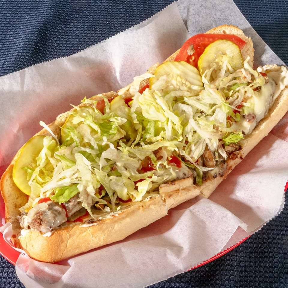 Zeda's Pizza cheesesteak sub with melted cheese, shredded lettuce, tomatoes, and pickles.