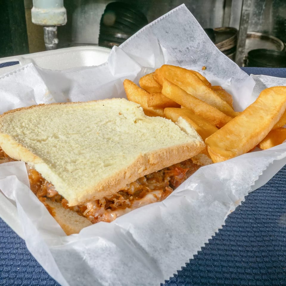 A Zeda's Pizza sandwich with meat and cheese, served with golden fries in a white paper-lined basket.