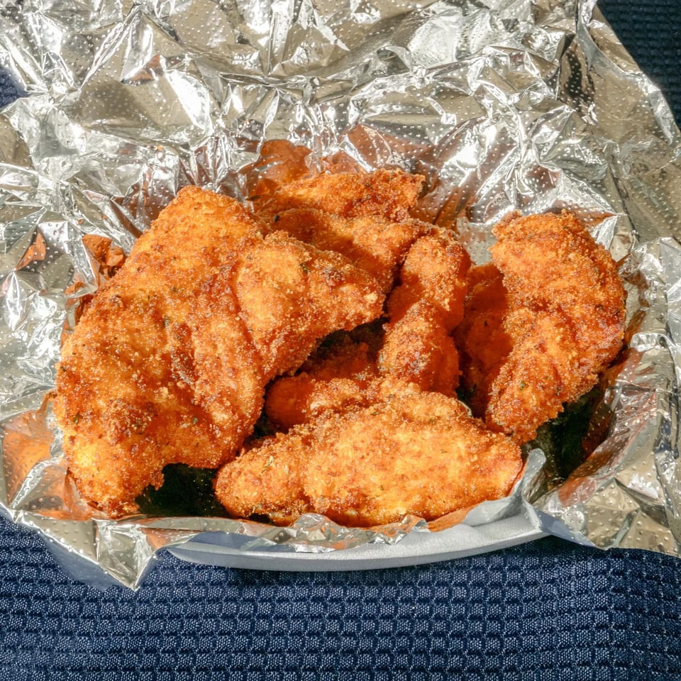 Golden-brown fried chicken tenders from Zeda's Pizza, served in a foil-lined container.