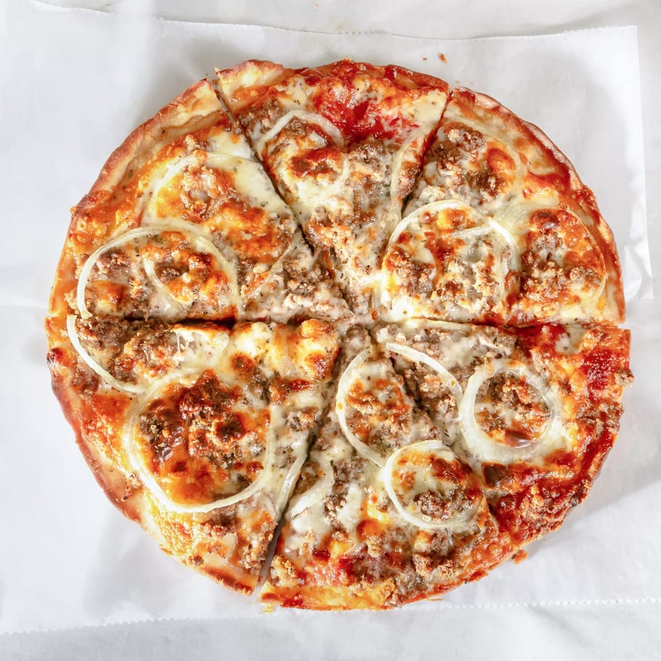 Zeda's Pizza with ground meat, melted cheese, and onion slices, cut into eight pieces.