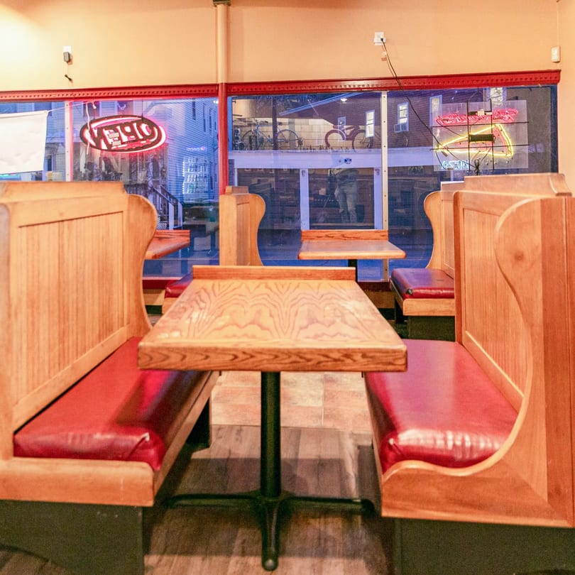 Interior of Zeda's Pizza with empty wooden booths, red cushions, and neon signs visible through the window.