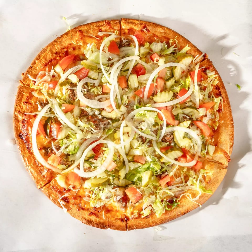 Zeda's Pizza with lettuce, tomatoes, onions, pickles, and ground beef on a white surface.