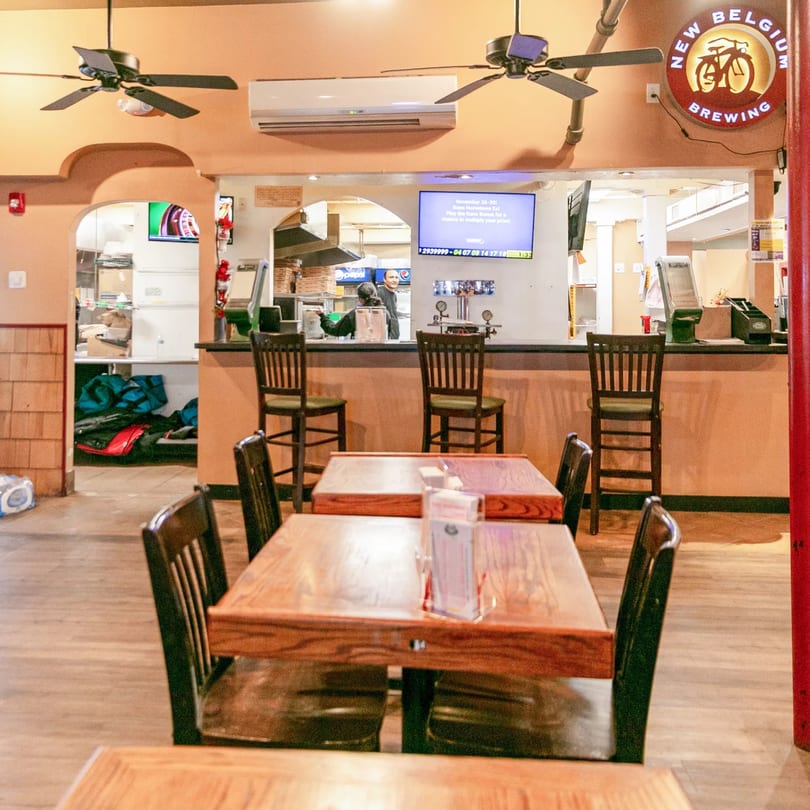 Interior of Zeda's Pizza with wooden tables, chairs, a counter, and a "New Belgium Brewing" sign.